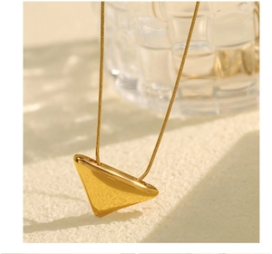 Detail of minimalist 18k gold plated triangle pendant on a textured cream background