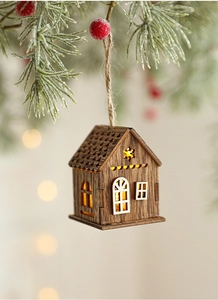 Primo piano di una casetta di Natale in legno illuminata appesa a un ramo di pino vero