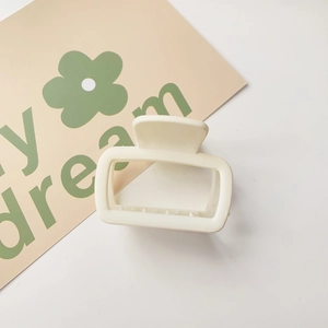 Detail of square matte cream hair claw clip with spring mechanism on a soft background