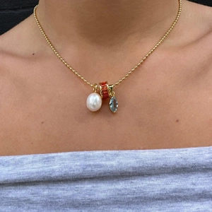 Close-up of gold beaded necklace with white pearl, blue gem and orange ring charms
