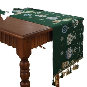 Dark green Christmas table runner with bell patterns and colorful tassels on wood
