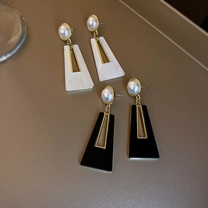 Detail of geometric acrylic earrings with golden frame and pearl studs in black and white