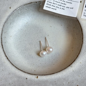 Macro shot of minimalist freshwater pearl earrings with 925 silver needles on ceramic plate
