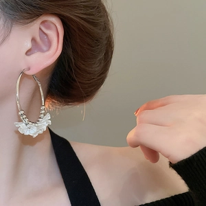 Detailed view of silver hoop earrings featuring white acrylic floral charms on model