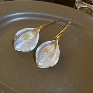 Détail de boucles d'oreilles lis calla blanc nacré avec crochets dorés sur plat céramique