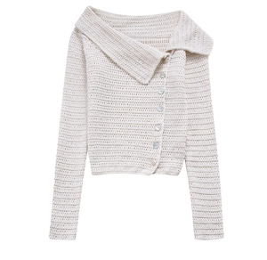 Dettaglio del cardigan in maglia bianco crema con trama spessa e bottoni asimmetrici