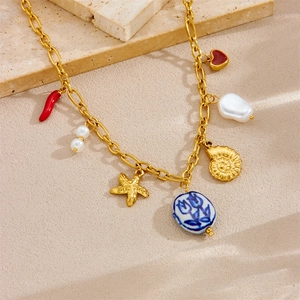 Vintage gold-plated necklace featuring star, pearl, chili, and shell charms on a flat lay surface