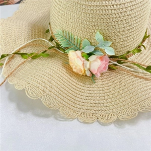 Close-up of wavy brim straw hat with pink floral decorations and natural weaving texture