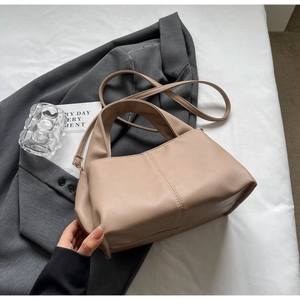Detail of lychee textured leather bag with top handle on a grey blazer backdrop