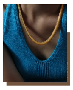 Detailed view of a flat gold-plated snake chain necklace on a blue knit vest