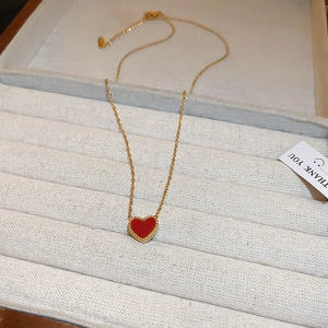 Vue détaillée d'un collier en chaîne dorée avec un pendentif cœur rouge dans un coffret