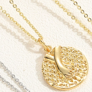 Macro detail of 14K gold plated medallion necklace with hand holding relief pendant
