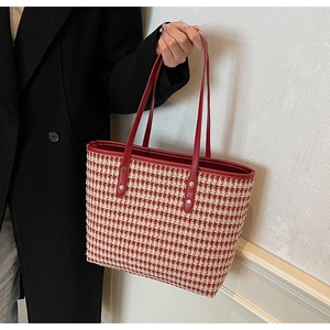 Detail of red houndstooth tote bag with leather straps and gold rivets held by a model
