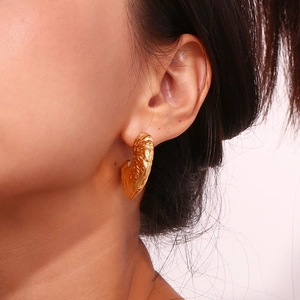 Detailed view of gold plated fan-shaped earrings with hammered texture on model