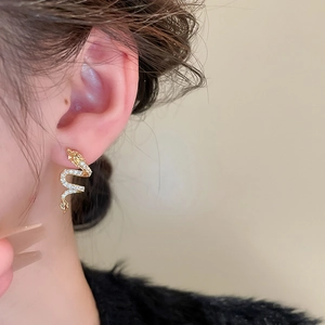 Close-up of golden dragon stud earrings with shimmering zircons worn by a model