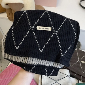 Close-up of a thick knit scarf with black and white diamond patterns and hand made label