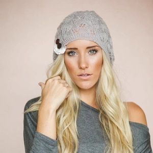 Close-up of grey knitted beanie featuring leaf hollow pattern and lace button detail