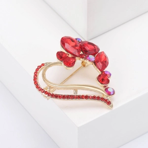Macro detail of a gold heart brooch with red crystals on a white geometric surface
