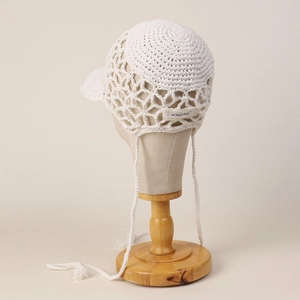 Detail of white handmade crochet baseball cap with ear flaps and delicate knit texture