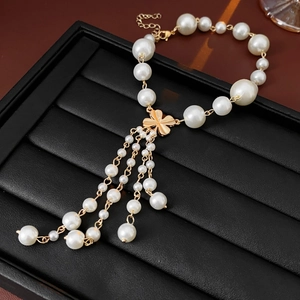 Detail of faux pearl bracelet featuring a golden clover charm and delicate tassels