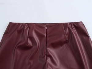 Detail view of burgundy PU leather shorts waist featuring a hidden zipper and glossy texture