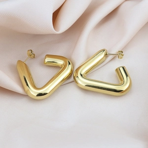 Detail view of gold hollow geometric textured hoop earrings on a soft pink satin fabric