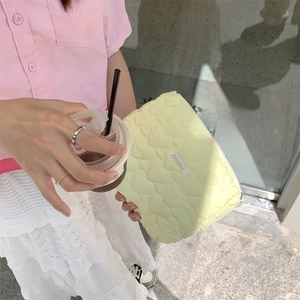 Detail of light yellow heart-quilted cosmetic bag held by a model in casual setting