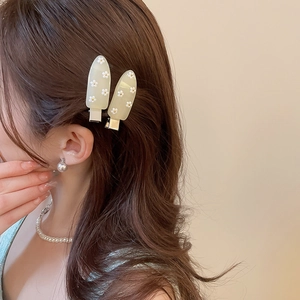 Detail of light green drop-shaped hair clips with white daisy patterns on a model's hair