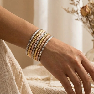 Detail of stacked gold, silver, and rose gold bracelets with diamond-cut patterns