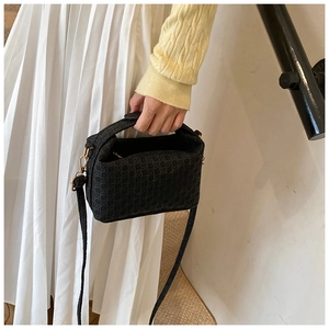 Detail of black woven texture handbag with golden hardware and long shoulder strap