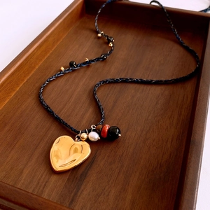 Détail du pendentif cœur doré sur un collier en corde tressée avec perles colorées