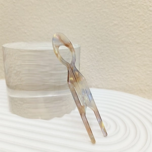 Close-up of marbled acetate U-shaped hair fork on a water-textured glass pedestal