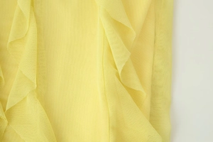 Close-up of bright yellow mesh fabric with layered ruffle details and fine lace texture