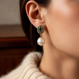 Detail of vintage gold earrings with green emerald stones and white pearls on a model