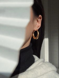 Close-up of chunky gold-plated oval hoop earrings with artistic cinematic shadow lighting