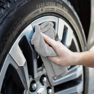 Absorbent grey microfiber cleaning cloth wiping a car alloy wheel rim effectively