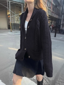 Close-up of black chunky knit cardigan with large brown buttons and front pockets