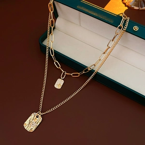 Detail of layered gold square pendant necklace with small crystal inlays on jewelry box