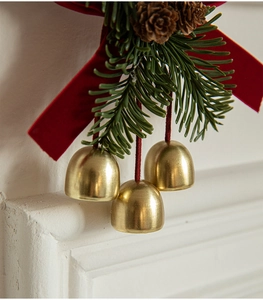 Detail of golden bells with a red velvet bow and green pine branches for Christmas decor