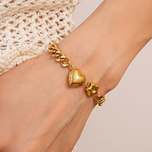 Detail of gold Cuban chain bracelet with heart, star, and flower charms on a wrist