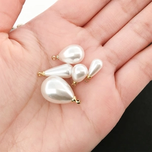 Golden teardrop faux pearl pendants in various sizes held on palm for DIY jewelry