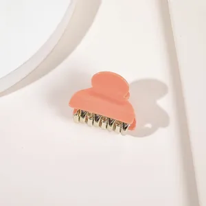 Detailed view of a small coral pink acrylic hair claw clip with silver metal teeth