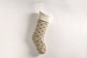 Detailed close-up of a beige knitted Christmas stocking with fish scale pattern and white cuff