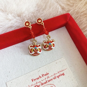 Détail de boucles d'oreilles lion chinois en émail rouge avec pompons dorés et perles