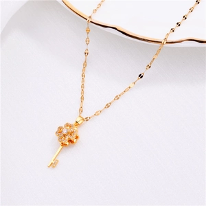 Detailed view of a gold clover key necklace with micro-paved zircons on a white fabric
