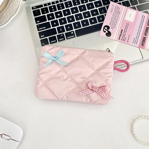 Detailed top view of pink quilted cosmetic bag with ribbon bows on a desk