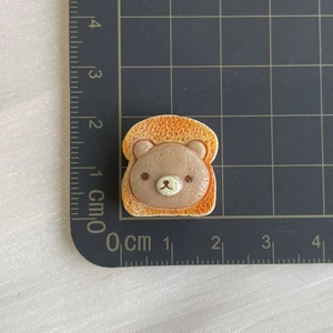 Macro shot of resin bear head bread charm showing 2cm size scale on a cutting mat