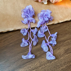 Detail of purple chiffon flower earrings with beaded tassels on vintage wood background