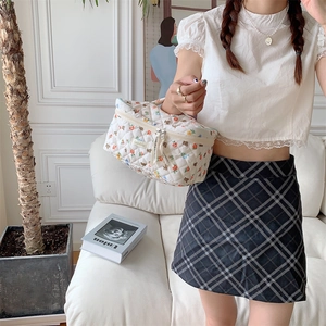 Quilted white cosmetic bag with floral bear patterns held by a hand in a home setting