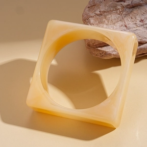 Detail of amber acrylic square bangle on stone, showcasing retro resin geometric texture